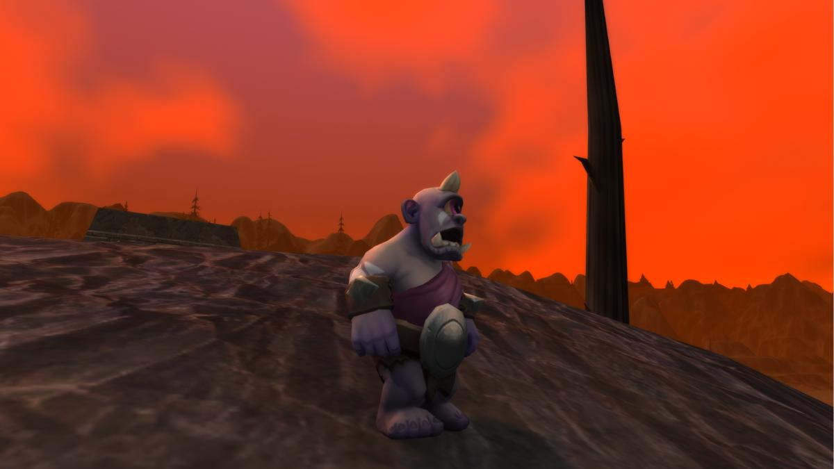 A small, cyclopean ogre stands against the backdrop of a burning wasteland