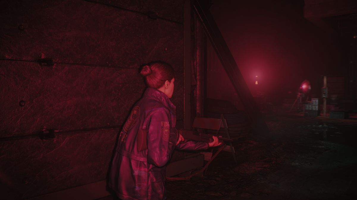 Kiran Estevez stands with a shotgun in a creepy room lit with red