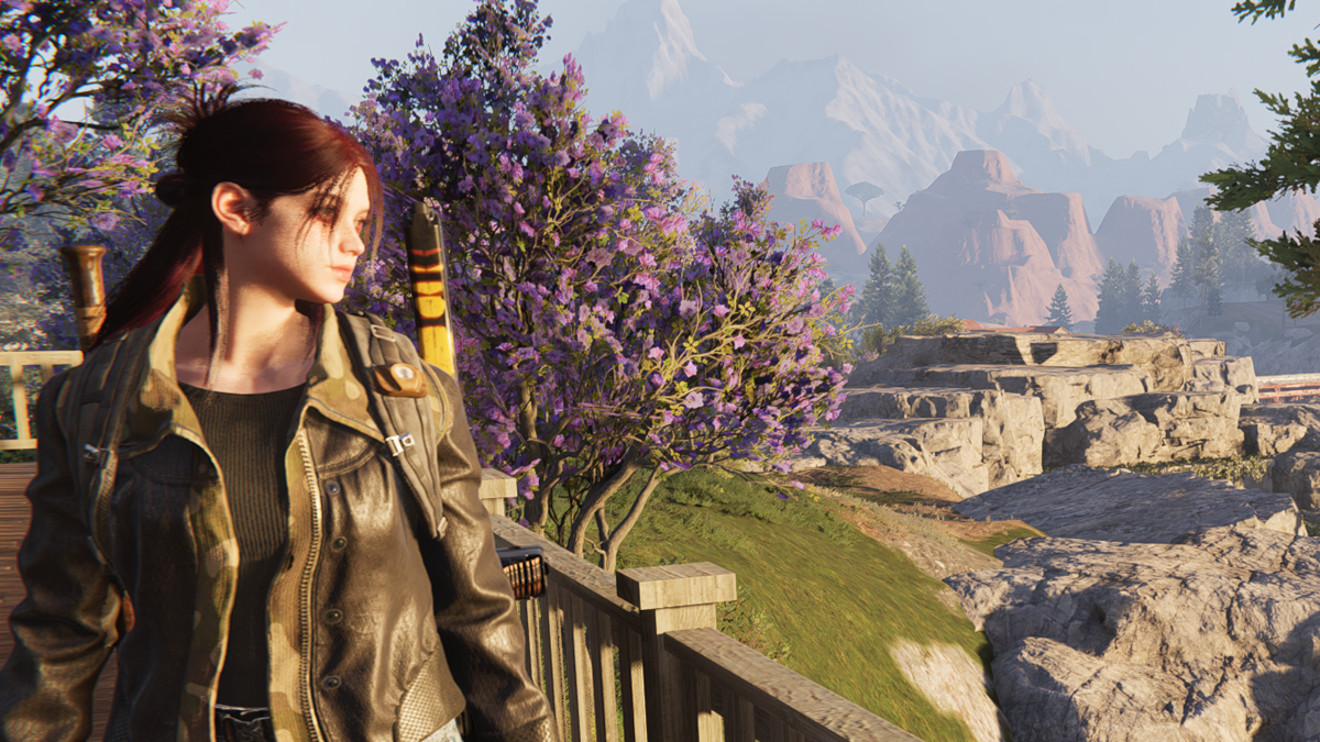 A girl looking over a balcony with trees and mountains in the background.