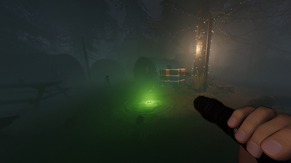 Phasmophobia: the player shines a flashlight at a green light in the center of a foggy campsite.