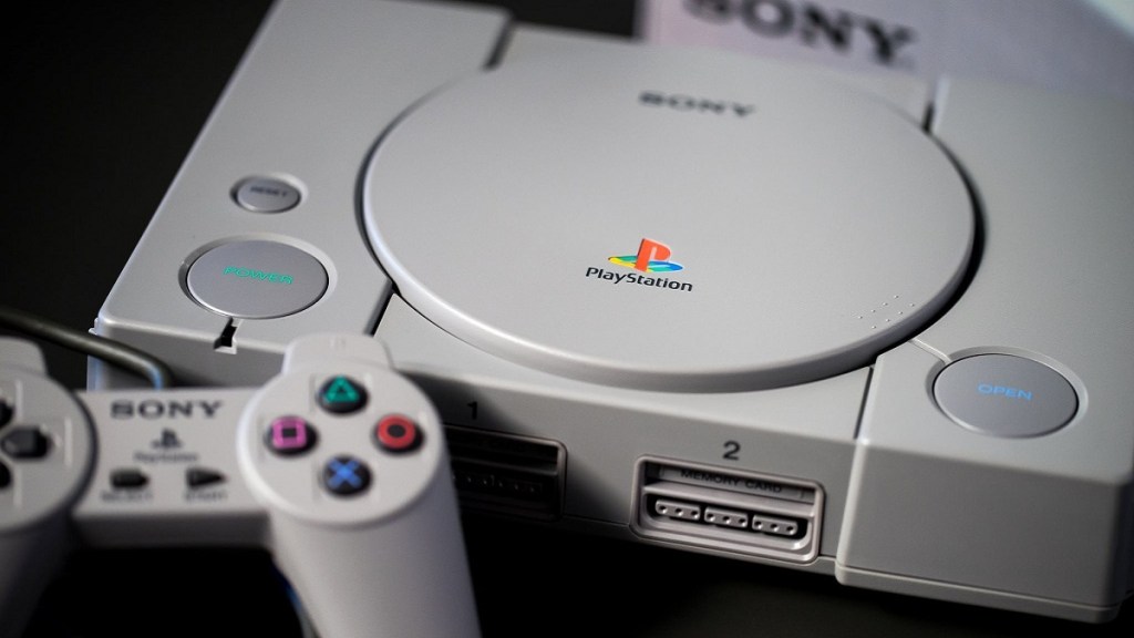 A gray Sony PlayStation and controller on a black background.