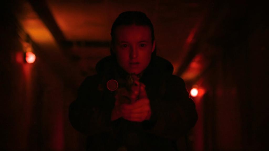 TLOU Show Ellie in red lighting, holding a gun