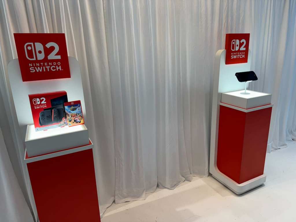 Nintendo Switch 2 box and Mario Kart World box on a stand, with the Nintendo Switch 2 console in handheld mode on another stand