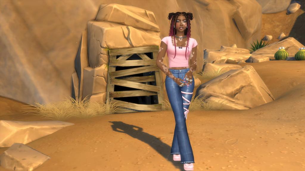 A Sim wearing a pink top and blue jeans standing in front of a cave in the sims 4
