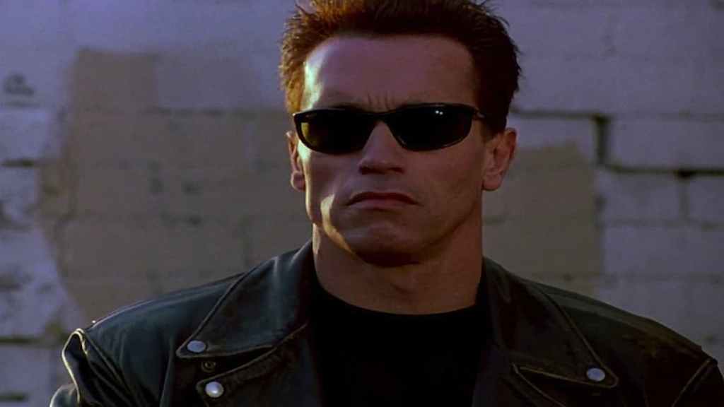 Arnold Schwarzenegger wearing sunglasses and a leather jacket while menacingly staring beyond the camera in Terminator 2: Judgement Day. 