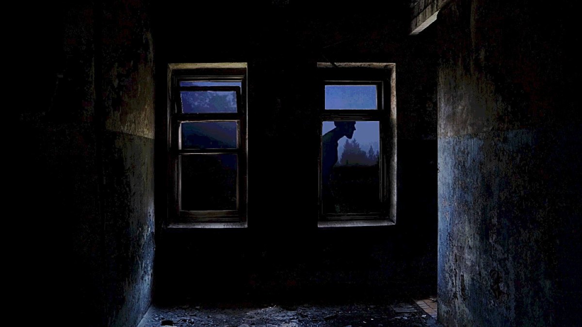 A dark shot inside a corridor, looking at two windows, with the silhouette of a Visitor passing by outside