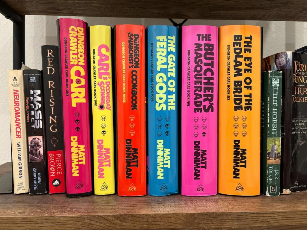 A photograph of the Dungeon Crawler Carl books in a row on a shelf. They all have brightly colored texts and spines.