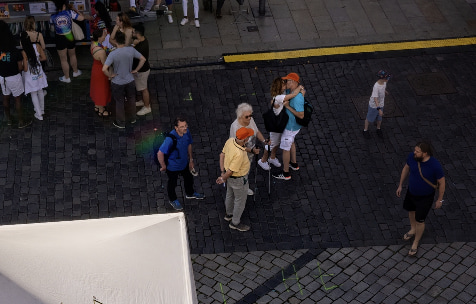 A man and a woman, surrounded by other people, kiss on a street in the middle of an event.