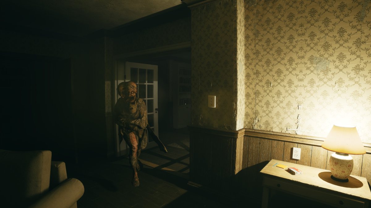 A female monster with head split in half and restrained, following protagonist in dimly lit room